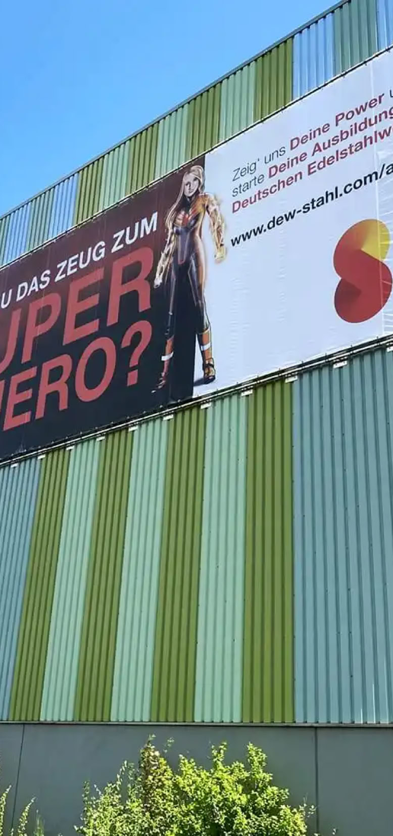 Werbeplakat an einer gestreiften Gebäudewand mit der Aufschrift "Hast du das Zeug zum Super Hero?" und einem Logo der Swiss Steel Group.