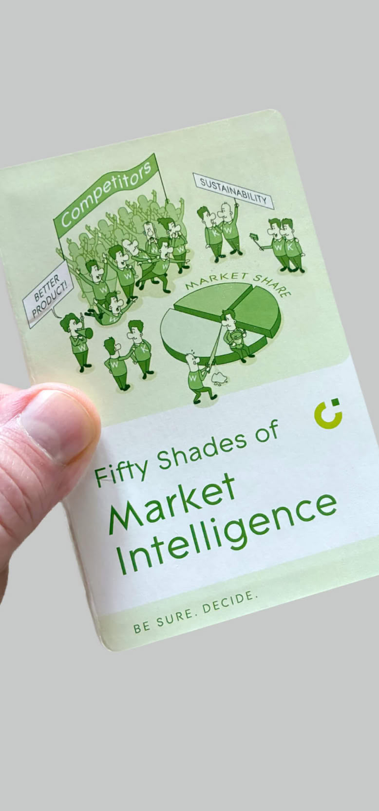 Eine Hand hält eine Karte mit der Aufschrift "Fifty shades of Market Intelligence" und einer Illustration von Menschen und einem Tortendiagramm.